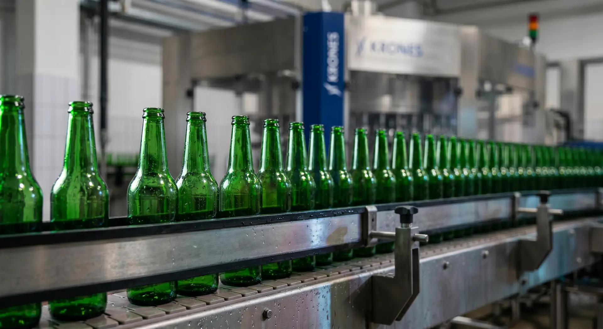 Grüne Flaschen auf einem nassen, wasserfesten Förderband in der Brauerei Kompania Piwowarska in Posen, im Hintergrund eine Krones-Maschine.